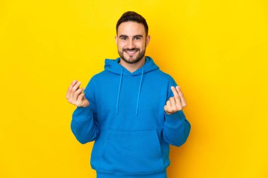 Sarı arka planda izole genç beyaz yakışıklı adam para hareketi yapıyor.