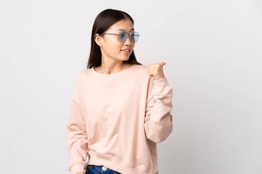 İzole edilmiş beyaz arka planı olan genç bir Çinli kız bir ürün sunmak için kenarı işaret ediyor.