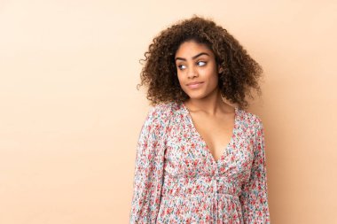 Genç Afrikalı Amerikalı kadın bej arka planda izole edilmiş. Şüpheli hareketler yapıyor.