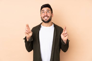 Beyaz tenli yakışıklı adam bej arka planda izole edilmiş, şans diliyor ve en iyisini diliyor.