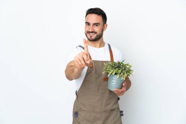 Bahçıvan elinde bir bitki tutuyor. Beyaz arka planda izole edilmiş. Parmağını kaldırıp gösteriyor.