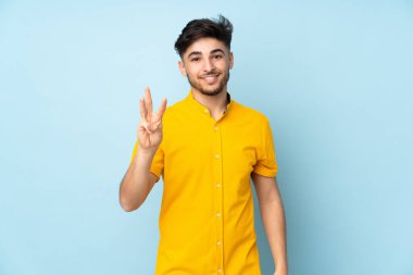 Soyutlanmış geçmişi olan yakışıklı Arap bir adam mutlu ve parmaklarıyla üçe kadar sayıyor.