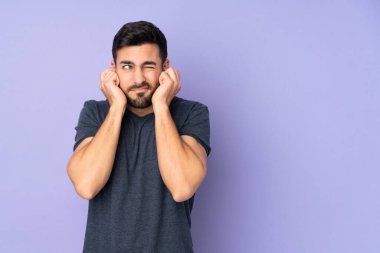 Kafkasyalı yakışıklı adam hayal kırıklığına uğramış ve mor arka plan yüzünden kulaklarını kapatmış.