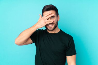 Beyaz tenli yakışıklı adam mavi arka planda izole edilmiş, gözleri kapalı ve gülümsüyor.