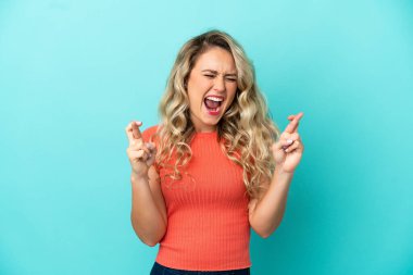 Genç Brezilyalı kadın mavi arka planda izole edilmiş, parmakları çapraz