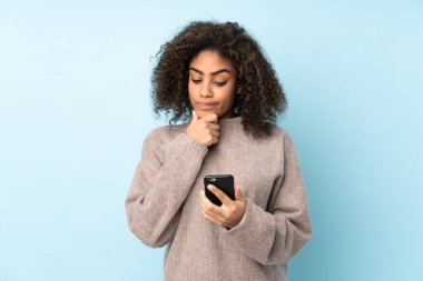 Genç Afrikalı Amerikalı kadın mavi arka planda izole edilmiş düşünüyor ve bir mesaj gönderiyor.