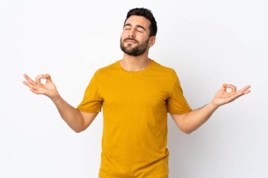 Sakallı yakışıklı bir genç, beyaz arka planda, zen pozunda.