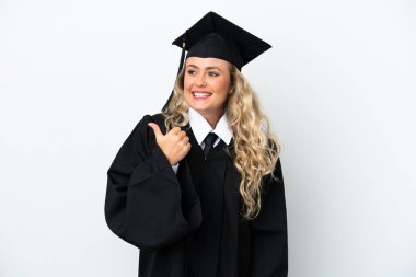 Üniversiteden mezun genç bir kadın beyaz arka planda izole edilmiş bir şekilde bir ürün sunmak için kenarı işaret ediyor.