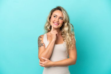 Genç Brezilyalı bir kadın mavi arka planda izole edilmiş bir şekilde yukarı bakarken bir fikir düşünüyor.