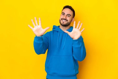 Sarı arka planda izole edilmiş beyaz tenli yakışıklı adam parmaklarıyla 10 'a kadar saydı.