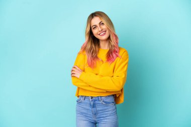 İzole edilmiş mavi arka planda genç bir kadın kollarını ön cephede çapraz tutuyor.