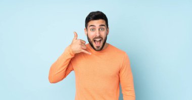 Beyaz tenli yakışıklı adam telefon jesti yapıyor. Beni geri ara. İzole edilmiş mavi arkaplanı imzala.