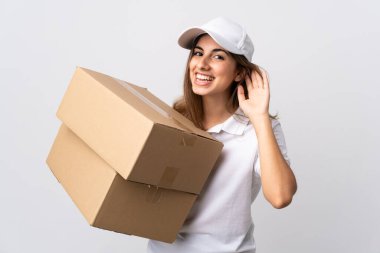 Genç teslimatçı kadın, izole edilmiş beyaz arka planda. Kulağına elini sürerek bir şeyler dinliyor.