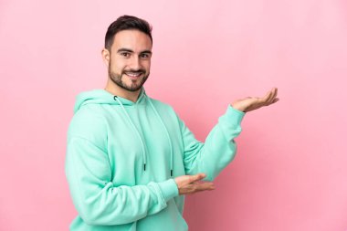 Pembe arka planda soyutlanmış beyaz tenli yakışıklı adam davet edildiği için ellerini yana uzatıyor.