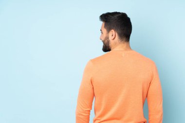 Beyaz tenli yakışıklı adam arka tarafta ve mavi arka plana bakıyor.