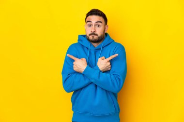 Sarı arka planda izole edilmiş beyaz, yakışıklı genç bir adam. Yan taraftakilerin şüphelerine işaret ediyor.