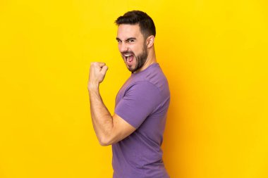 Sarı arka planda izole edilmiş beyaz yakışıklı bir adam zaferi kutluyor.