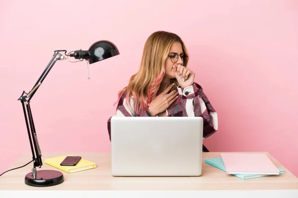 Young student woman in a workplace with a laptop over pink background coughing a lot