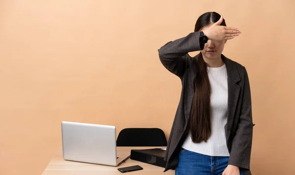 Chinese business woman in her workplace covering eyes by hands