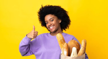 Genç Afrikalı Amerikalı bir kadın sarı arka planda izole edilmiş bir ekmek alıyor.