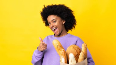 Genç Afrikalı Amerikalı bir kadın sarı arka planda izole edilmiş bir şeyler alıyor. Önü işaret ediyor ve gülümsüyor.