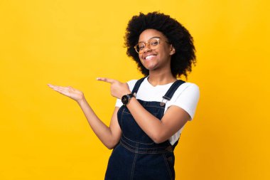 Sarı arka planda izole edilmiş genç Afrikalı Amerikalı bir kadın. Avucunun içinde hayali bir ilan tutuyor.