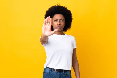 Sarı arka planda izole edilmiş genç Afrikalı Amerikalı kadın dur hareketi yapıyor.