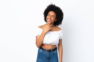Beyaz arka planda izole edilmiş genç Afrikalı Amerikalı kadın gülümserken yukarı bakıyor.