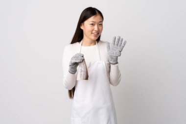 Çinli balıkçı önlük takıyor ve çiğ bir balığı izole edilmiş beyaz arka planda tutuyor mutlu bir ifadeyle selamlıyor.