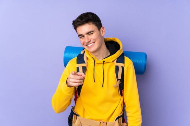 Mor arka planda izole edilmiş büyük bir sırt çantası olan Kafkasyalı genç bir dağcı.