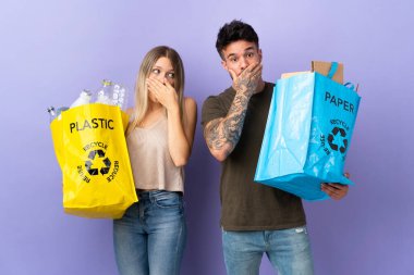 Mor arka planda izole edilmiş, ağzı ellerle kapatan beyaz bir çift uygunsuz bir şey söyledi diye geri dönüşüm yapıyor.