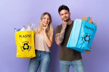 Mor arka planda izole edilmiş, tatlı bir ifadeyle gülümseyen beyaz bir çift geri dönüşüm yapıyor.