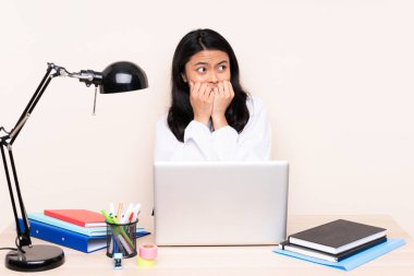 İş yerindeki Asyalı öğrenci bilgisayarlı bir kız bej arka planda izole edilmiş gergin ve eli ağıza vermeye korkuyor.