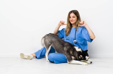 Sibiryalı Husky köpeği olan veteriner doktor yerde gururlu ve kendini beğenmiş bir şekilde oturuyor.