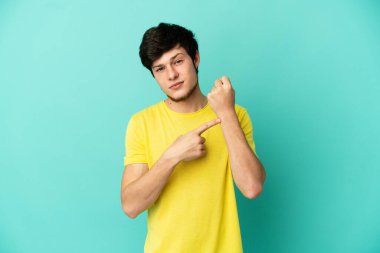 Genç Rus adam mavi arka planda izole edilmiş, geç kalma hareketi yapıyor.