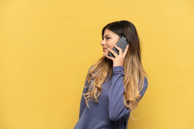 Sarı arka planda izole edilmiş cep telefonu kullanan genç Rus kız.