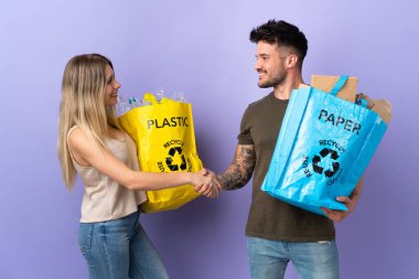 Genç beyaz çift, mor arka planda izole edilmiş bir şekilde geri dönüşüm yapıyor.