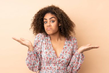 Genç Afrikalı Amerikalı kadın, bej arka planda izole edilmiş, şüpheli hareketler yapıyor.