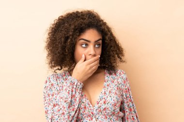 Genç Afrikalı Amerikalı kadın bej arka planda izole edilmiş. Yan tarafa bakarken sürpriz jest yapıyor.