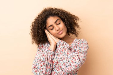 Genç Afrikalı Amerikalı kadın bej arka planda izole edilmiş. Uyku jesti yapıyor.