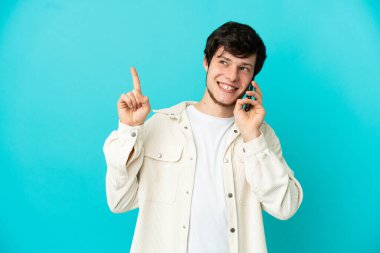 Mavi arka planda izole edilmiş cep telefonu kullanan genç bir Rus harika bir fikre işaret ediyor.