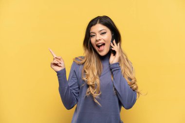 Sarı arka planda izole edilmiş cep telefonu kullanan genç bir Rus kızı çözümü bulmak için parmağını kaldırıyor.