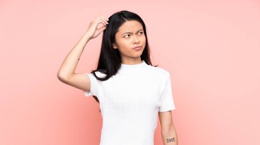 Genç Çinli bir kadın pembe arka planda izole edilmiş. Kafasını kaşırken şüpheleri var.