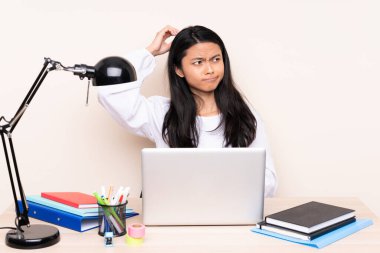 İş yerinde bej arka planda dizüstü bilgisayarı olan Asyalı bir kız öğrencinin kafası kaşınırken şüpheleri var.