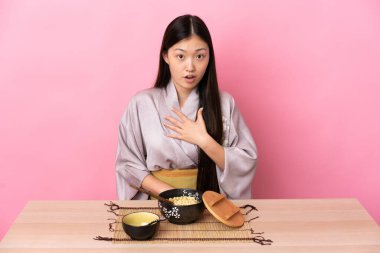 Kimono giyen ve erişte yiyen genç Çinli kız şaşırmış ve şaşırmış.