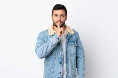 Beyaz arka planda sakallı yakışıklı genç adam sessiz bir jest işareti gösteriyor. Parmağını ağzına sokuyor.