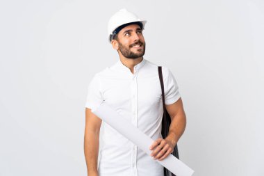 Miğferli ve elinde planları olan genç bir mimar beyaz arka planda izole edilmiş bir şekilde yukarı bakarken bir fikir düşünüyor.