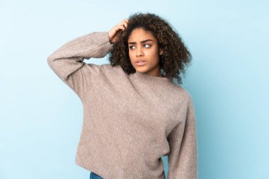 Genç Afrikalı Amerikalı kadın mavi arka planda izole edilmiş. Kafası kaşınırken şüpheleri var.