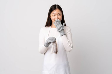 Çinli balıkçı önlük takıyor ve soyutlanmış beyaz arka planda çiğ balık tutuyor mutlu ve ağzı eliyle kaplayan gülümsüyor.