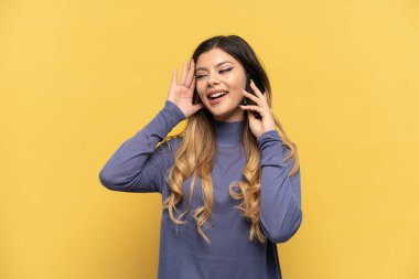 Sarı arka planda izole edilmiş cep telefonu kullanan genç Rus kız kulağına elini sürerek bir şeyler dinliyor.
